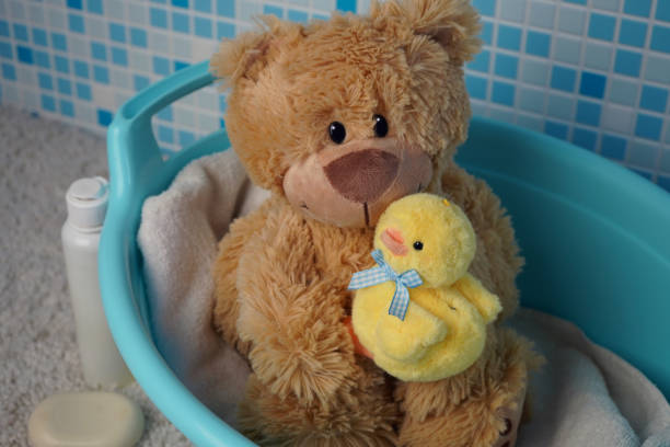 Teddy bear with a yellow duck in a blue bath basin.