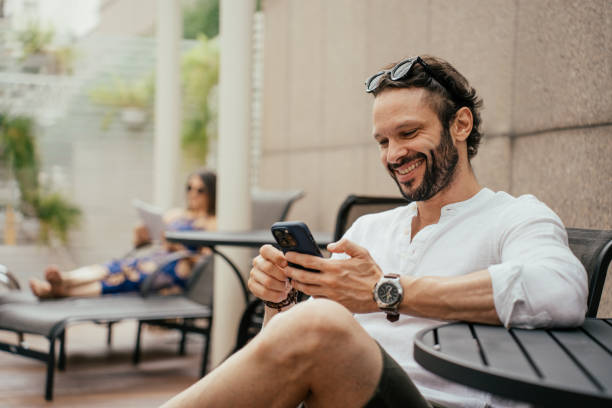người đàn ông thư giãn bên hồ bơi bằng điện thoại thông minh - affluent lifestyles hình ảnh sẵn có, bức ảnh & hình ảnh trả phí bản quyền một lần