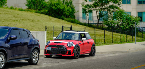 Brantford, Ontario, Canada- June 4, 2024. Chili red colour MINI COOPER on urban street  in downtown Branford, Ontario, Canada. Mid summer day. This is the third generation model F56 JCW, since BMW took over iconic brand of MINI. MINI featured in the photo is John Cooper Works model, the most powerful 2 door version. This compact car features engine build and designed by BMW, and packs even more power and torque than previous models, since 2002 to present. Original design clues and themes are still present on this brand new model. Mini has been around since 1959 and has been owned and issued by various car manufacturers.