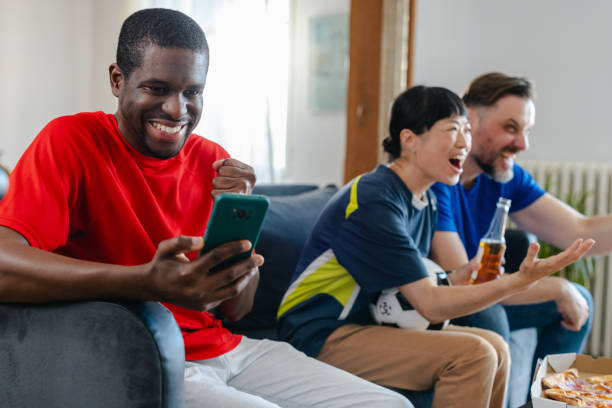 istock Cheerful African American young man using smart phone while watching sports with friends 2157455602