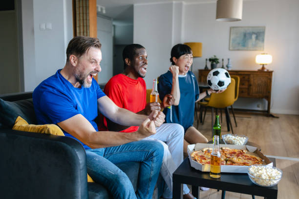 istock Three soccer fans sitting on a couch  and watching game on TV 2157456607