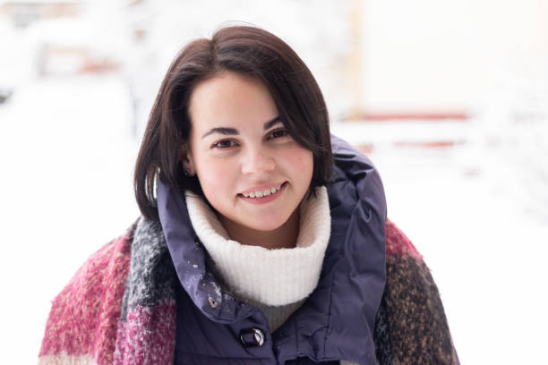 istock Young smiling beautiful woman wearing scarf outdoors during snowfall 2157467264