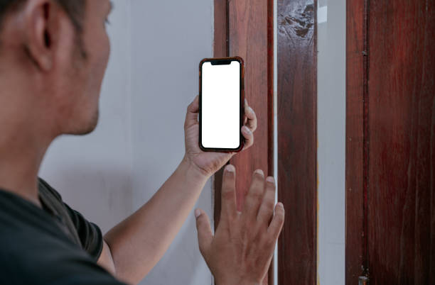 istock Asian man holding smart phone with mockup white blank display, empty screen for app ads, standing at living room. 2157468692