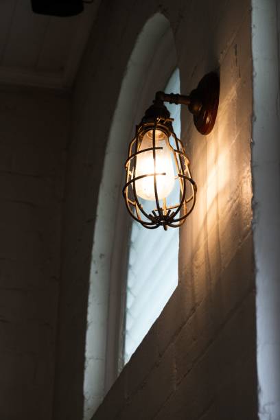 istock Vintage wall-mounted light fixture illuminating a brick wall next to an arched window 2157473909
