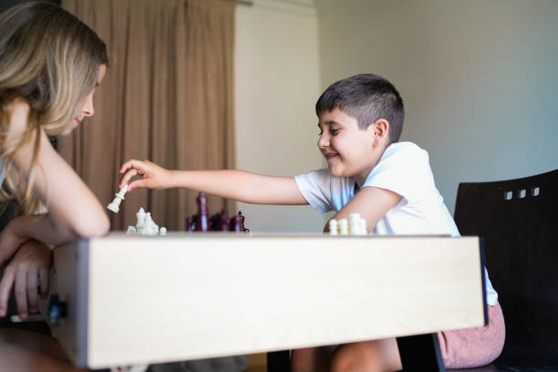 A boy and a girl are playing chess. The boy is smiling and the girl is looking at the board
