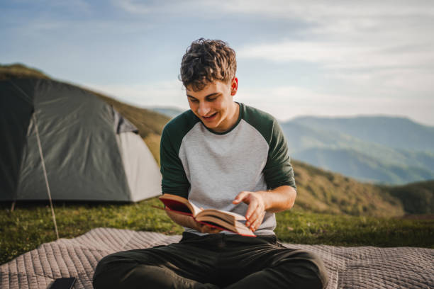 istock Young boy read a book on the mountain in front tent 2157488981