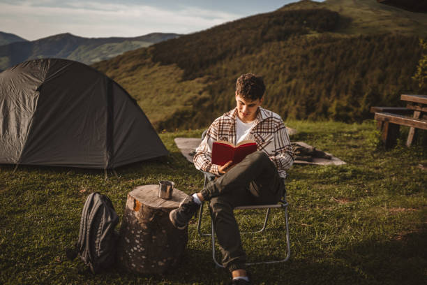 istock Young boy sit in front tent read a book on the mountain 2157489175