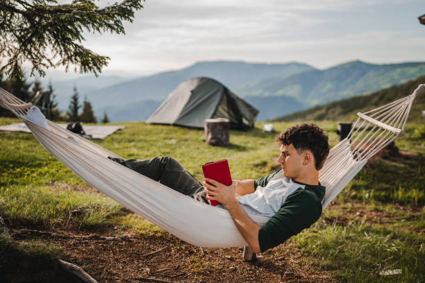 istock Young boy lying down in a hammock on the mountain and read a book 2157489263
