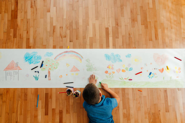 istock Boy lying on the floor and drawing with colorful crayons on a white paper 2157491540