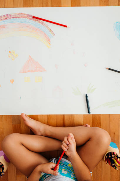 Above shot of child drawing with crayons on a paper on the floor