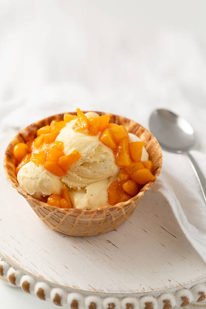 Fresh peaches top vanilla ice cream in a waffle bowl on a white background.