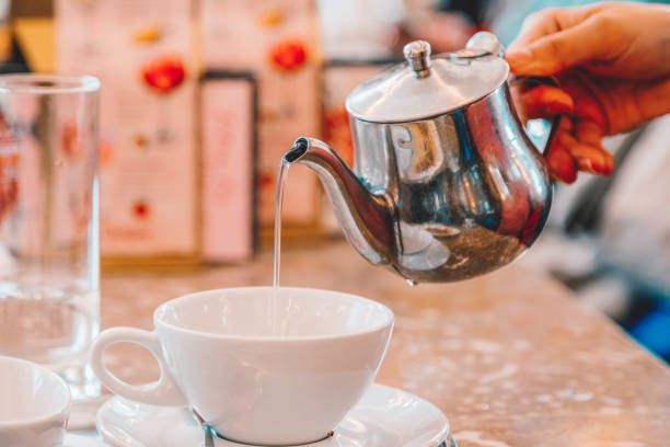 istock Hand Pouring Hot Water from a Teapot into a White Cup at a Cafe Table 2157499032