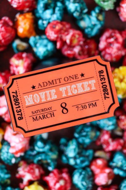 Stock photo showing close-up, elevated view of a movie ticket surrounded by red, blue, green, orange and yellow popcorn.