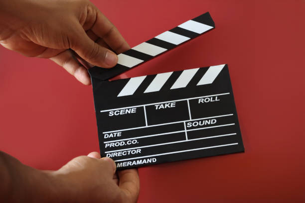Stock photo showing close-up view of a hinged clapper stick on a black film slate being clapped by an unrecognisable person.