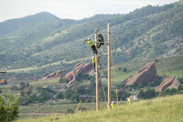 Lineman crews work on power lines high in the sky. An elevated hydraulic bucket lifts the workers up to the power line. Sunrise or sunset views.