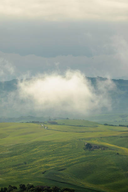 View of the enchanting atmosphere of Tuscany with this captivating scene of fog rolling over green hills on a rainy spring day. The mystical fog and dark weather create a hauntingly beautiful landscape, capturing the unique charm and allure of this iconic Italian region.