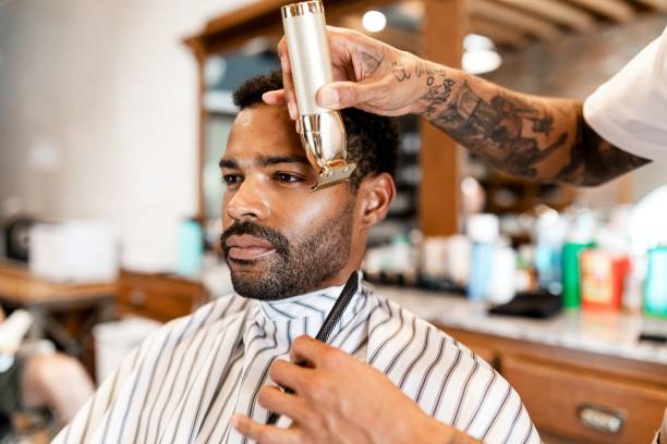 Side view of afro man with top hair loose and bottom section braided while stylist's hands continue creating African braids.