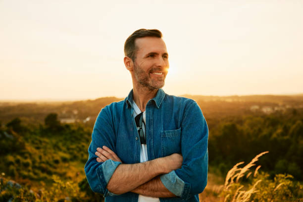 Portrait of smiling man standing outdoors while hiking during sunny weekend in nature Portrait of smiling adult man on day hike during sunset mid adult men stock pictures, royalty-free photos & images