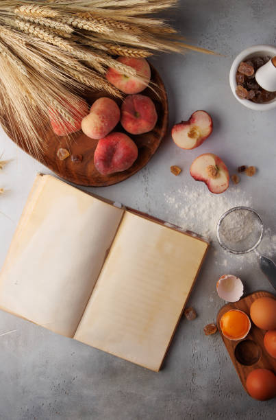 Around empty cookbook a set of peaches, flour and eggs on rustic gray concrete table, top view. High quality photo
