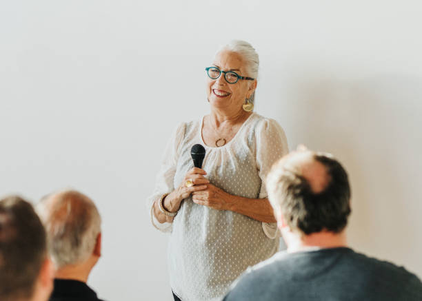 Cheerful elderly woman speaking on a microphone in a seminar