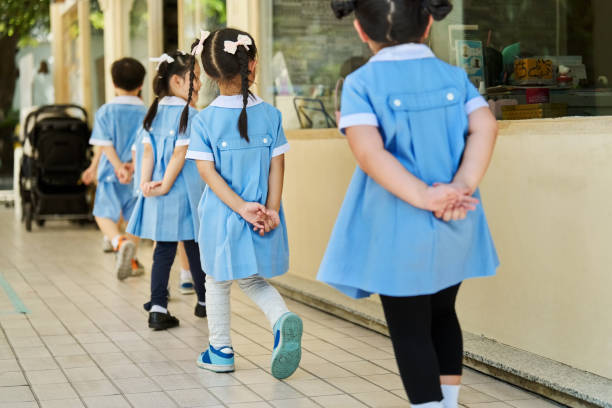 Rear view of preschool children walking neatly in line with hands behind their backs heading to the classroom