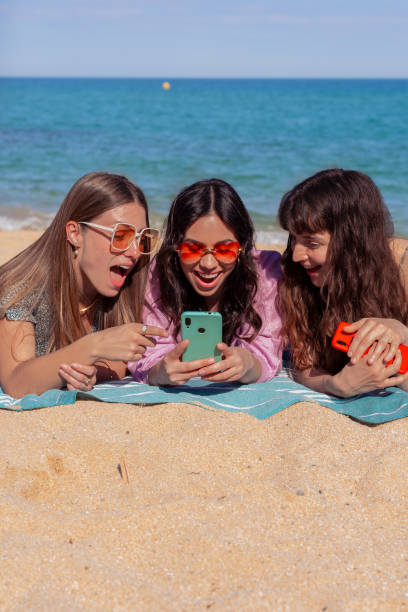istock Three happy young friends on the beach using apps on their smartphones.Vertical 2157558039