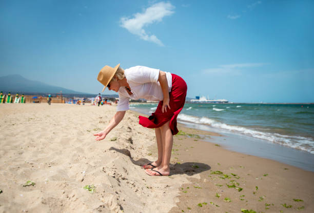 Senior Woman picking sea shells from the sand in sea beach in Catania, Sicily. Copy space
