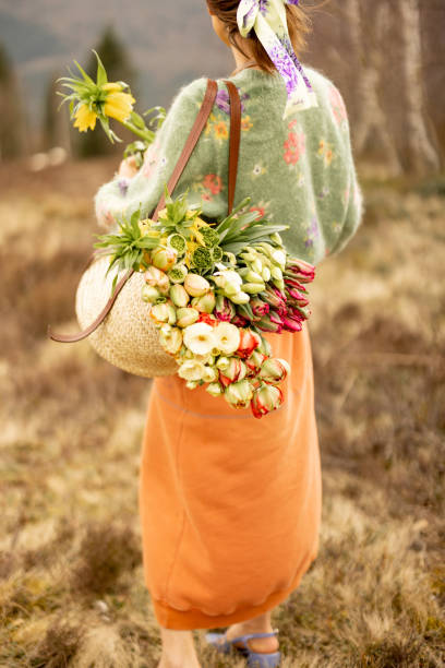 Portrait of a young woman in pink standing with bag full of colorful flowers on a beautiful meadow in mountains. Concept of beauty and carefree lifestyle on nature