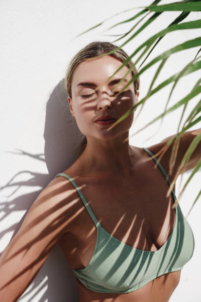 istock Young Woman in Green Bikini Posing with Palm Leaf on White Background 2157576410