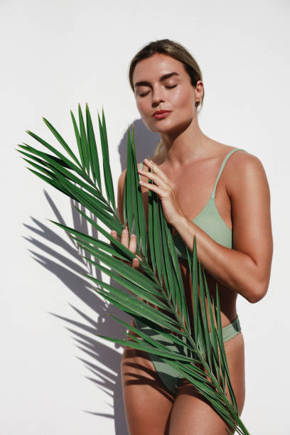 istock Young Woman in Green Bikini Posing with Palm Leaf on White Background 2157576969