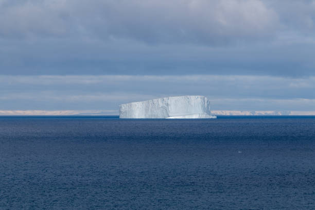 Huge Antarctica Tabular Iceberg with big natural ice arches and caves drifting on the Antarctic South Atlantic Ocean under blue sunny sky. Small Ice Floe Parts in the Foreground. Antarctic Ocean, Antarctica.