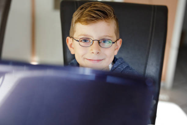 A cute elementary aged boy dressed in business attire working in a retro office setting at an old desktop computer.  Wood paneling on the walls.