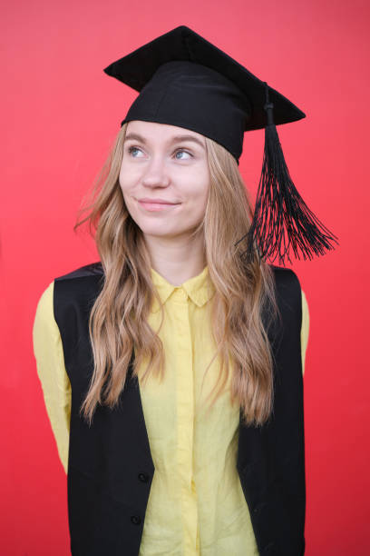 Young beautiful blond female in graduation cap with emotional facial expression on red background. Happy to finish school, college or university High quality photo
