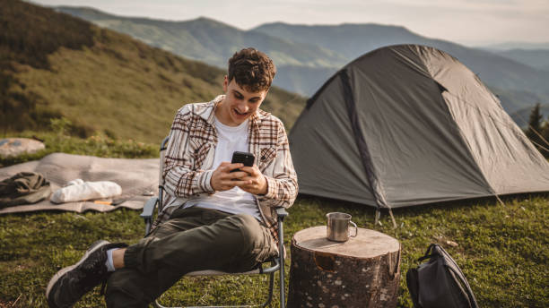 istock Young boy sit in front tent and use mobile phone on the mountain 2157580935