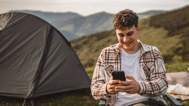 istock Young boy sit in front tent and use mobile phone on the mountain 2157581103