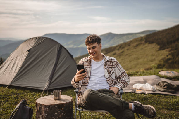 istock Young boy sit in front tent and use mobile phone on the mountain 2157581105