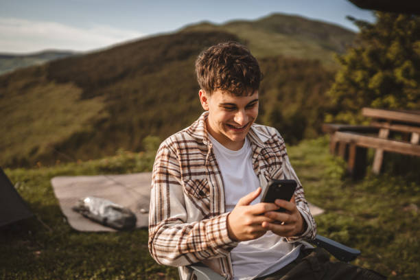 istock Young boy sit in front tent and use mobile phone on the mountain 2157581183