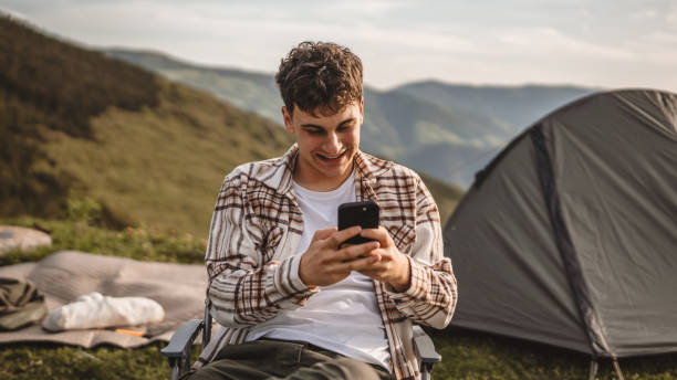 istock Young boy sit in front tent and use mobile phone on the mountain 2157581342