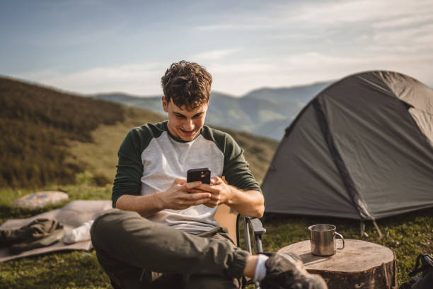 istock Young boy sit in front tent and use mobile phone on the mountain 2157581439
