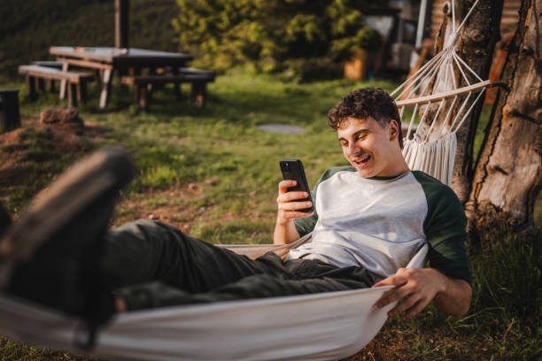 Young boy lying down in hammock and use mobile phone on the mountain
