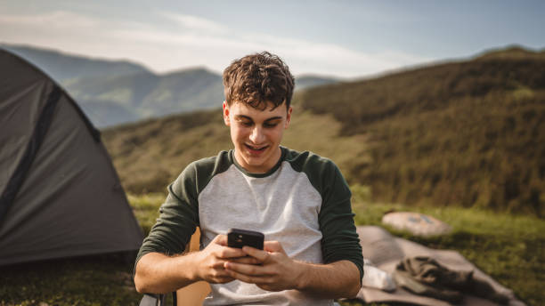 istock Young boy sit in front tent and use mobile phone on the mountain 2157581665