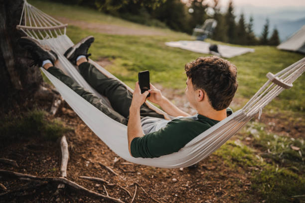 istock Young boy lying down in hammock and use mobile phone on the mountain 2157581834