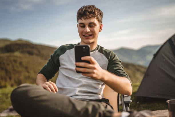 istock Young boy sit in front tent and use mobile phone on the mountain 2157581836