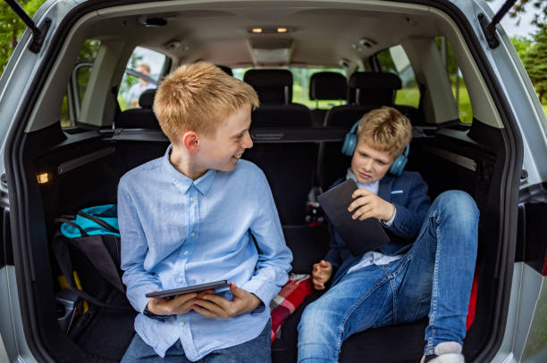 istock Caucasian schoolboys, using a digital tablet connected to a car WiFi, while sitting in a car trunk 2157585545