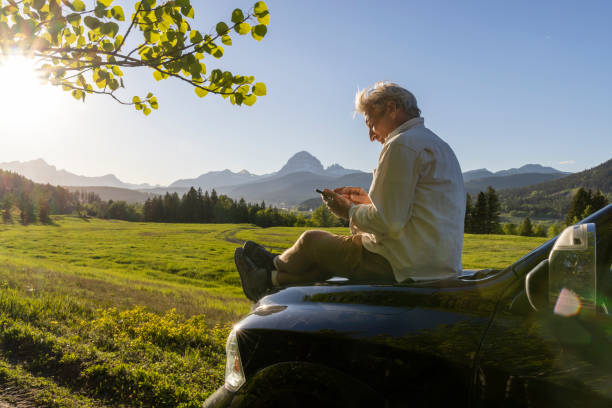 istock Senior man uses phone on vehicle in mountain meadow 2157587378