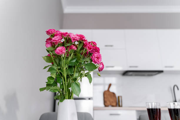 istock A white vase with small pink roses in the kitchen. White modern kitchen. Beautiful table setting. There are fruits, wine glasses and flowers on the table. 2157598635