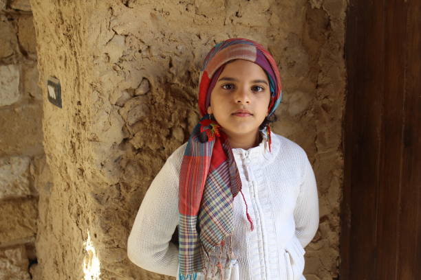 Beautiful young girl wearing white pullover leaning on a mud wall in Siwa in Egypt