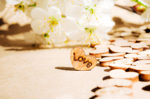 Wooden heart kraft paper background with text love sunlight Copy space Wedding invitation card Valentine Birthday Defocused bokeh effect Front side view Cherry brunch flowers Road of love Spring mood