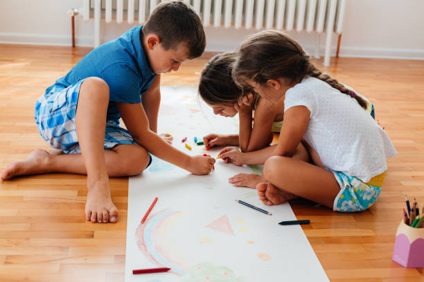 istock Creative children sitting on the floor and drawing with crayons on a paper 2157613373
