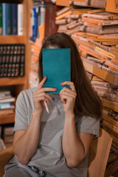 istock Woman Hiding Face With Book in a Library 2157616485